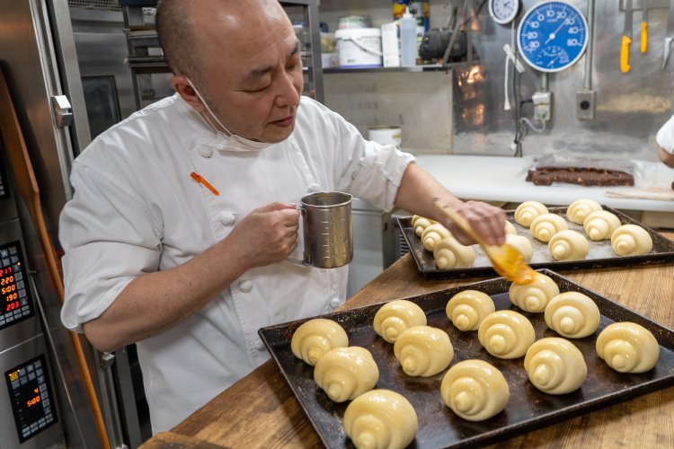 シェフの根本孝幸さん。焼成前のバターロールに卵液を塗る。