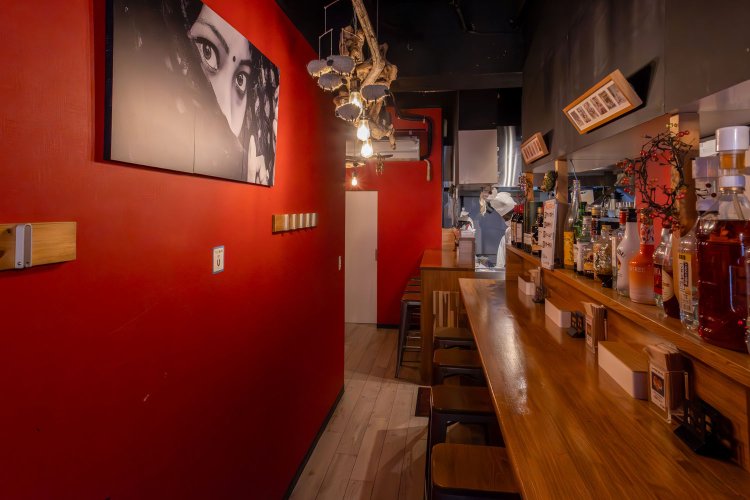 赤い壁にスタイリッシュなモノクロ写真が印象深い店内。カウンター席に加え奥と手前にはテーブル席もある。