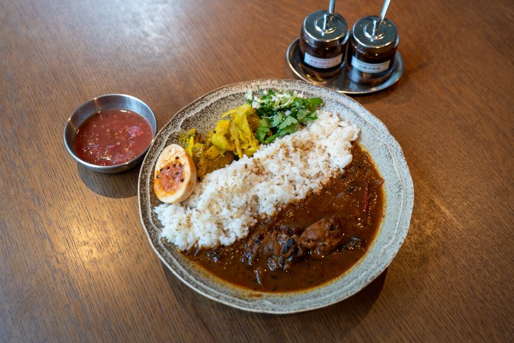 紅（AKA）は燻製唐辛子のスパイシーチキンカレー。左の小さな器は、トマトのアチャール。「激辛紅用」「激辛黒用」と書かれたスパイス瓶があり、そのひとさじでもっと辛くできる。