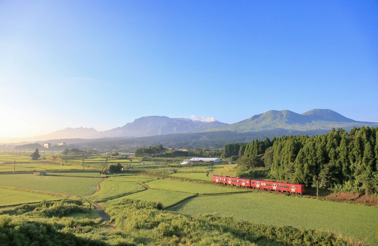 阿蘇五岳に赤い車体が映える。豊肥本線 内牧～阿蘇間（写真＝レイルマンフォトオフィス）。