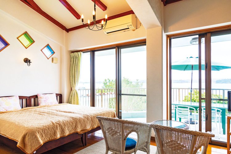 “わが家の別荘”気分でくつろげる空間が評価され、旅行新聞新社主催の2025年「日本の小宿」10 選の1つに。“古宇利ブルー”を横目にベッドでごろり。