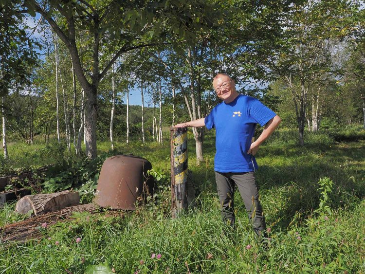 深名線現役時代から残る電信柱の遺構とオーナーの富岡達彦さん。天塩弥生駅はご夫婦で切り盛りされており、パートナーの方が駅長で富岡さんが主席助役だ。