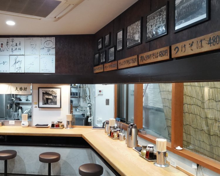 座席はカウンターのみ。壁には著名人のサインや白黒写真、昔のお品書き札が飾られている。