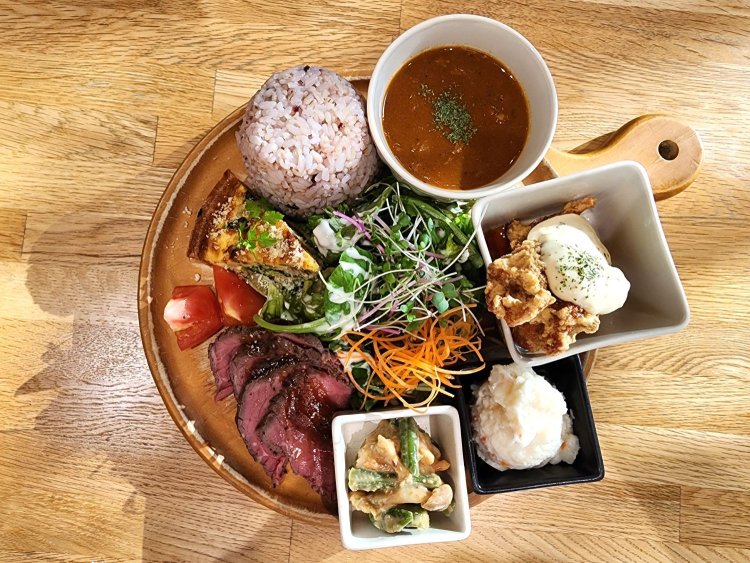 左上から右回りに五穀米、カレー、鶏の南蛮漬け、ポテトサラダ、いんげんと蒸し鶏のゴマ味噌和え、ローストビーフ、キッシュ。真ん中にグリーンサラダ。