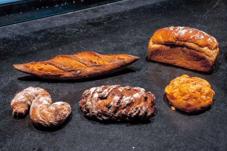 右上から時計回りに、オーガニック全粒粉40％、黒糖を使ったパンドミ・黒食476円。エメンタールとゴーダチーズにクミンが香るフロマージュ421円。クルミの香ばしさとクランベリーの果実感が満載のカカオルージュ1274円。クルミ、カシューナッツ、ピスタチオの異なる食感が楽しいノーチェ497円。味わい深い、オーガニック全粒粉100％のバゲット、ソル400円。