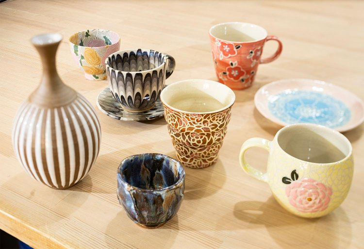 小岩の土で縞模様を描いた花器1万6500円など左の4点が信弘さん作。練り上げなど多様な技法を駆使。掻き落としで花を描いたカップ（中左、4400円）などの右4点が理子さん作。