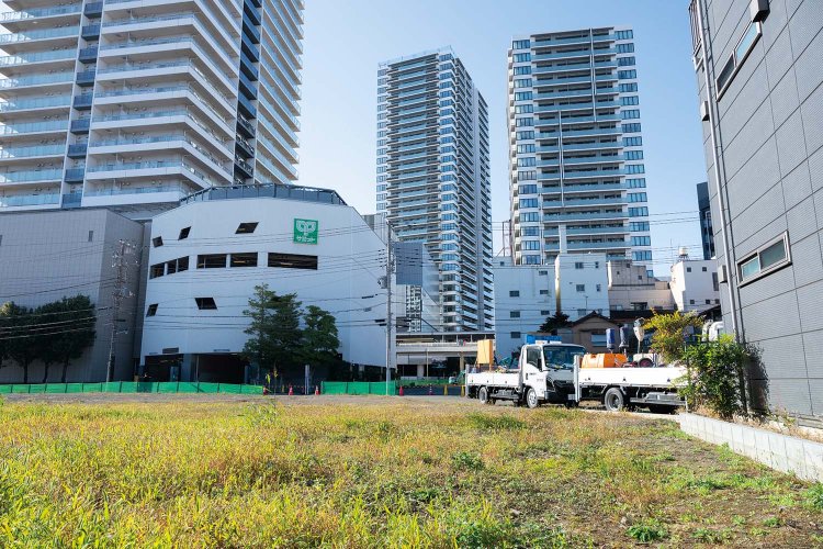 3棟（中央は竣工前）の高層マンションが建つフラワーロードの裏に、「リングロード」予定地が広がる（2025年11月撮影）。