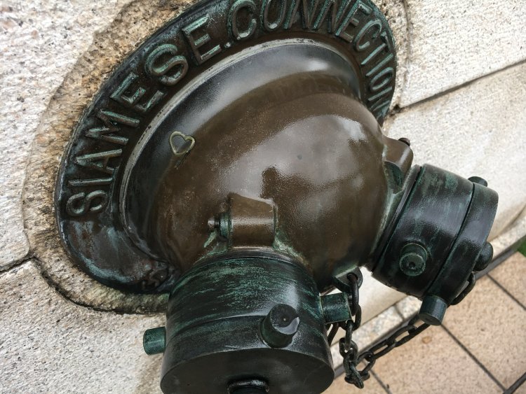 円盤状の飾り板に錆出し文字が印象的。村上製作所製の送水口。福井地方裁判所にて。