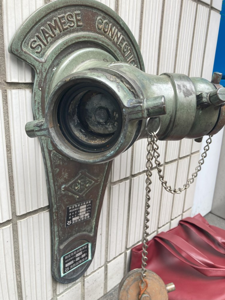 村上製作所とともに、日本の送水口草創期を牽引した建設工業社製の英字送水口。新橋センタープレイスにて。