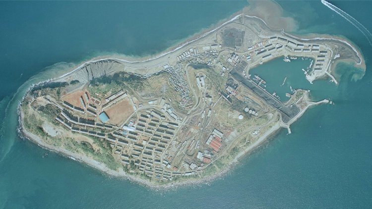 最盛期の頃の池島空中写真。池島港に隣接して黒い帯状のものが写っている。これは貯炭場で、石炭船が荷役している機械がトリンマー、その近くで貯炭場にブームが延びる機械がジブローダー。島の北側に軌道も見える。埋め立て地はボタ山の代わりであった。国土地理院『地図・空中写真閲覧サービス　国土地理院 コースC43 長崎1975年2月26日撮影』より拡大加工。