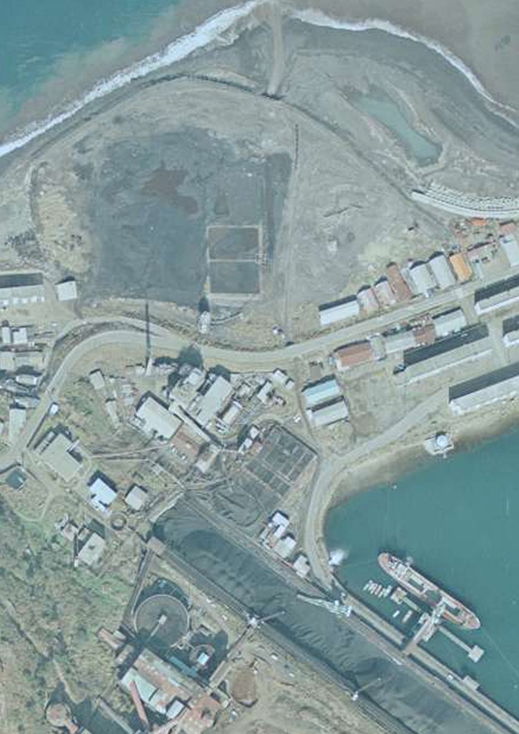 上記の空中写真を拡大してみると、軌道が道路をアンダーパスして海側に広がる埋め立て地（写真やや上側の広大な空き地）へと続いている。線路はうっすら確認できた。埋め立て地は「ボタ」と呼ばれる石炭の選炭で生じた岩石廃棄物を埋めたもの。国土地理院「地図・空中写真閲覧サービス　国土地理院 コースC43 長崎1975年2月26日撮影」より拡大加工。