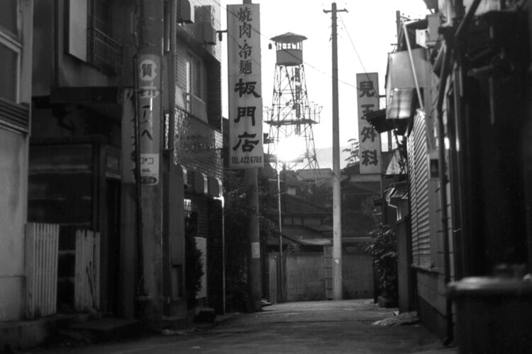 南口商店街中ほどから茶沢通り方面に抜ける路地。この路地には昔から何軒かの商店が店を構えていた。正面に世田谷消防署北沢出張所の火の見櫓が見える（1969年10月撮影）。