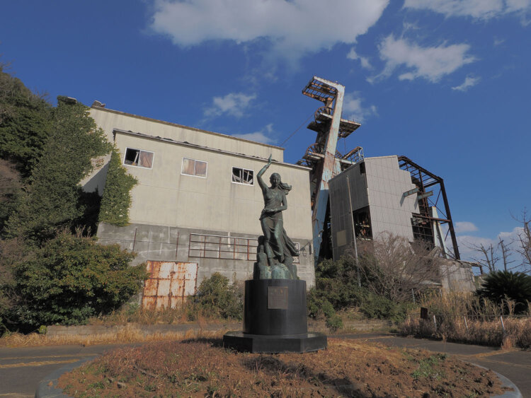 第2立坑の前には『慈海』のタイトルが命名された女神像が立ち、坑内安全を祈願していた。背後に立坑の巻上機と滑車が聳えている。