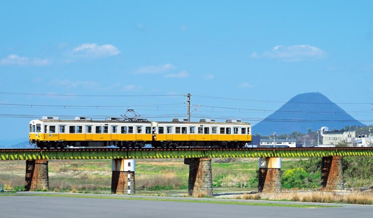 近代産業遺産の土器川橋梁を走る車両。後ろに見えるのは“讃岐富士”こと飯野山（写真＝マシマ・レイルウェイ・ピクチャーズ）。