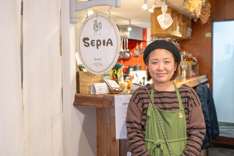 店長の川船亜貴子さん。「洋装セピア」の看板はカウンター横に掲げている。