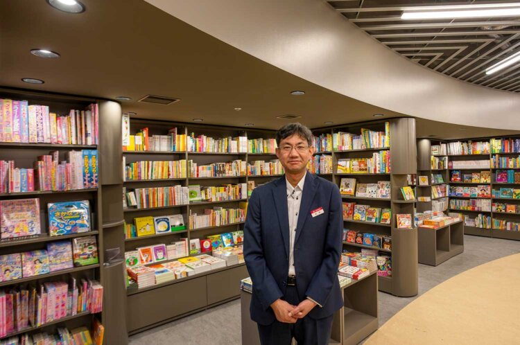 円形に書棚が並ぶ児童書の“洞窟”の前で、店長の杉本佳文さん。