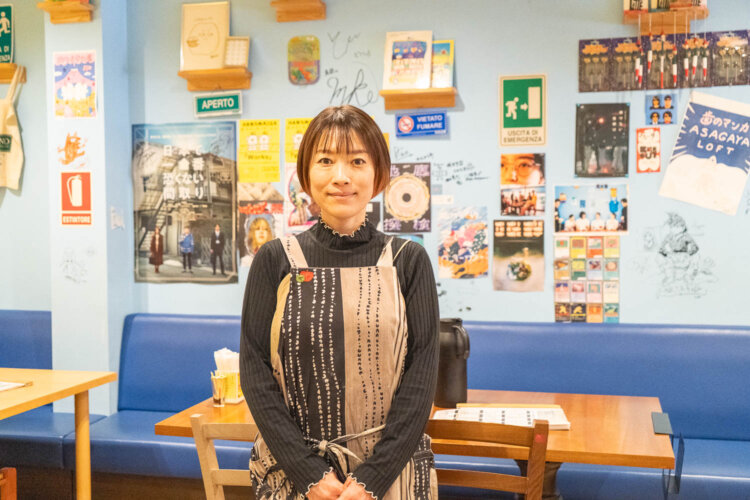 お店経営と子育てを両立する店主の安達鮎さん。壁のポスターはアルバイトスタッフが所属する劇団『南極』のものが多い。