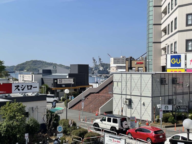 歩道橋ベイウォーク上からコースカベイサイドストアーズ方面を望む。チェーン店の看板の向こうに米軍の艦船が見える。