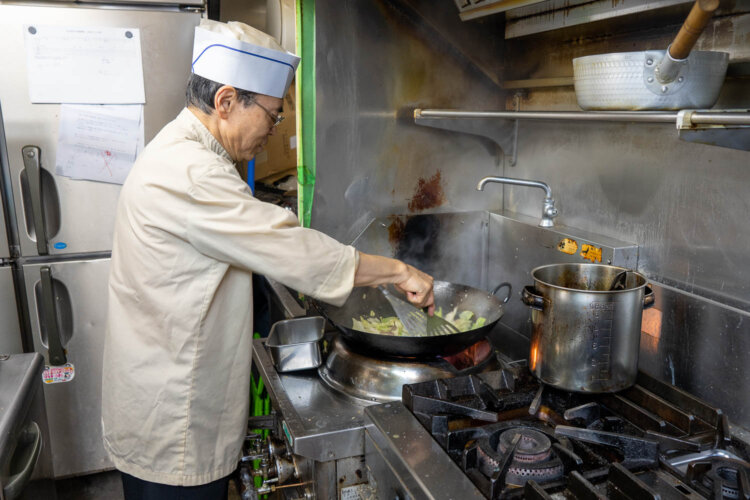 店主の石沢稔さん。肉とキャベツを炒めるとき、必ず両手でフライ返しを持つ。