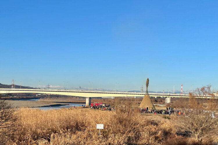 押立のどんど焼きの遠景。……え!? 多摩川にかかる「稲城大橋」より高いぞ、やぐらが！（2025年1月に撮影）。
