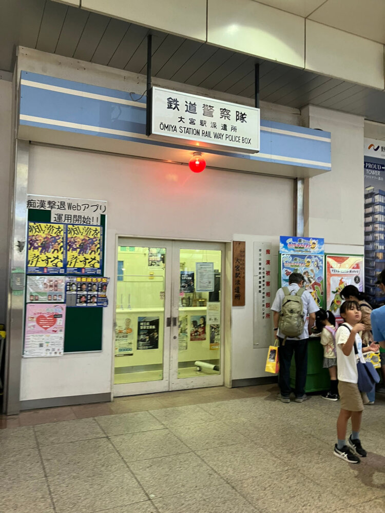 名標型案内板や木製モニュメントの向かいにある鉄道警察隊。多くの人が行きかう。
